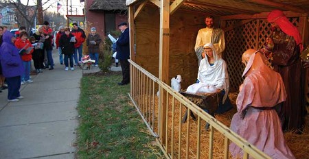A group from local churches stands before a life size nativity scene singing Christmas carols.